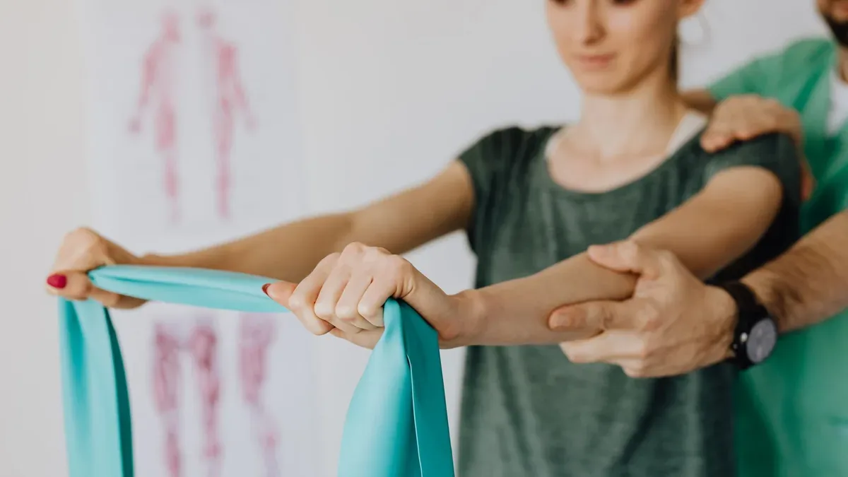 Fisioterapeuta ajudando paciente a levantar o braço com faixa elástica, dor no ombro ao levantar o braço